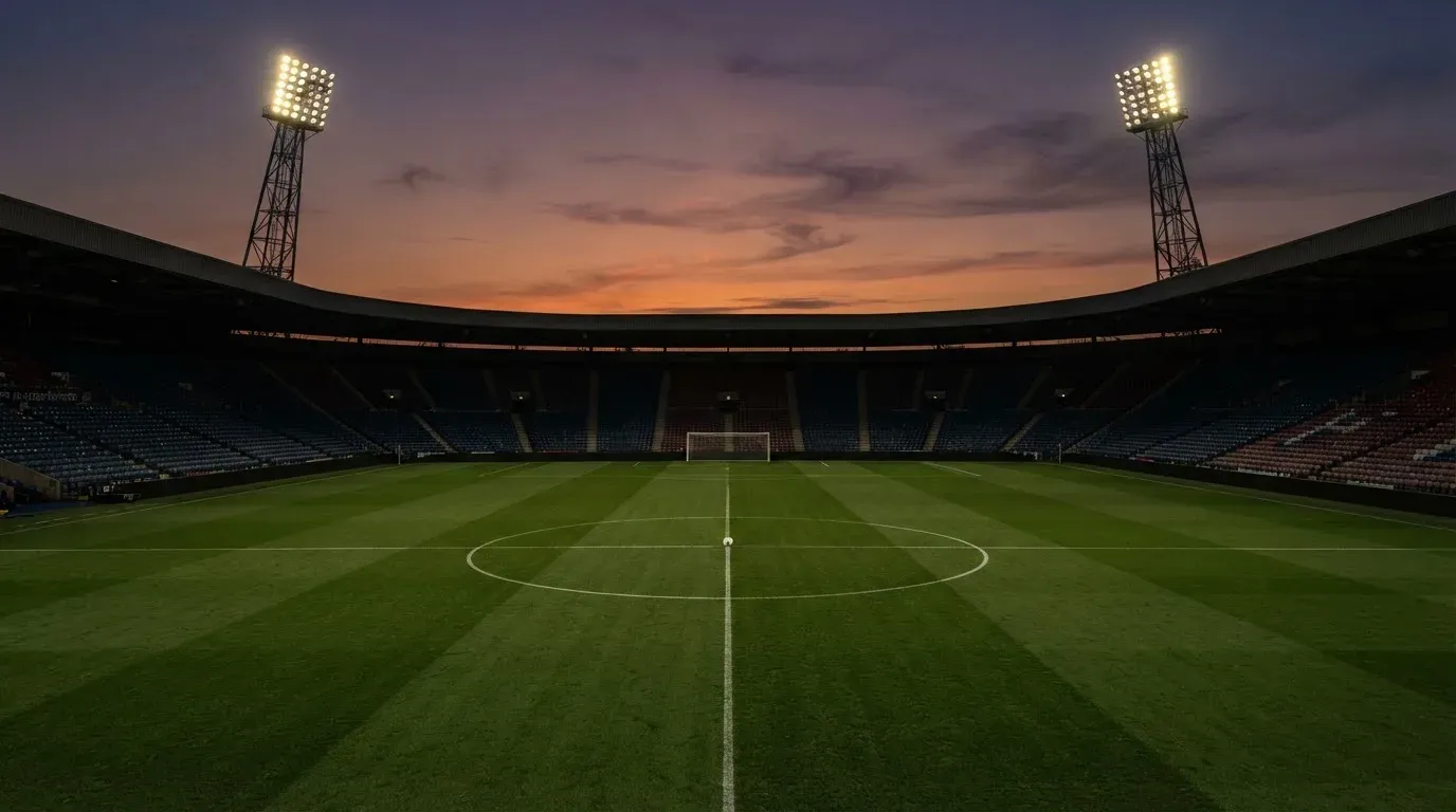 An empty football stadium with floodlight masts at dusk