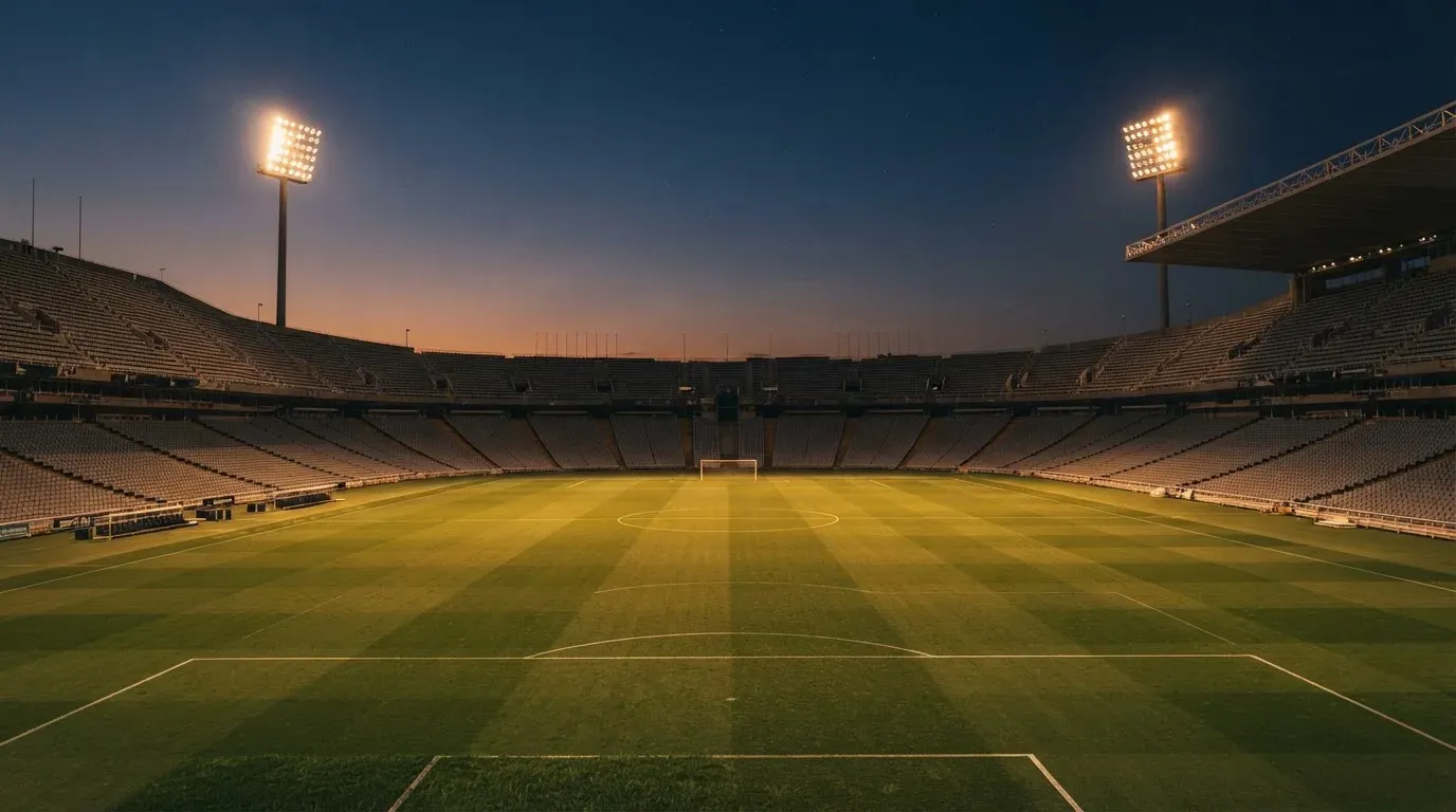 An empty football stadium with floodlight masts at dusk