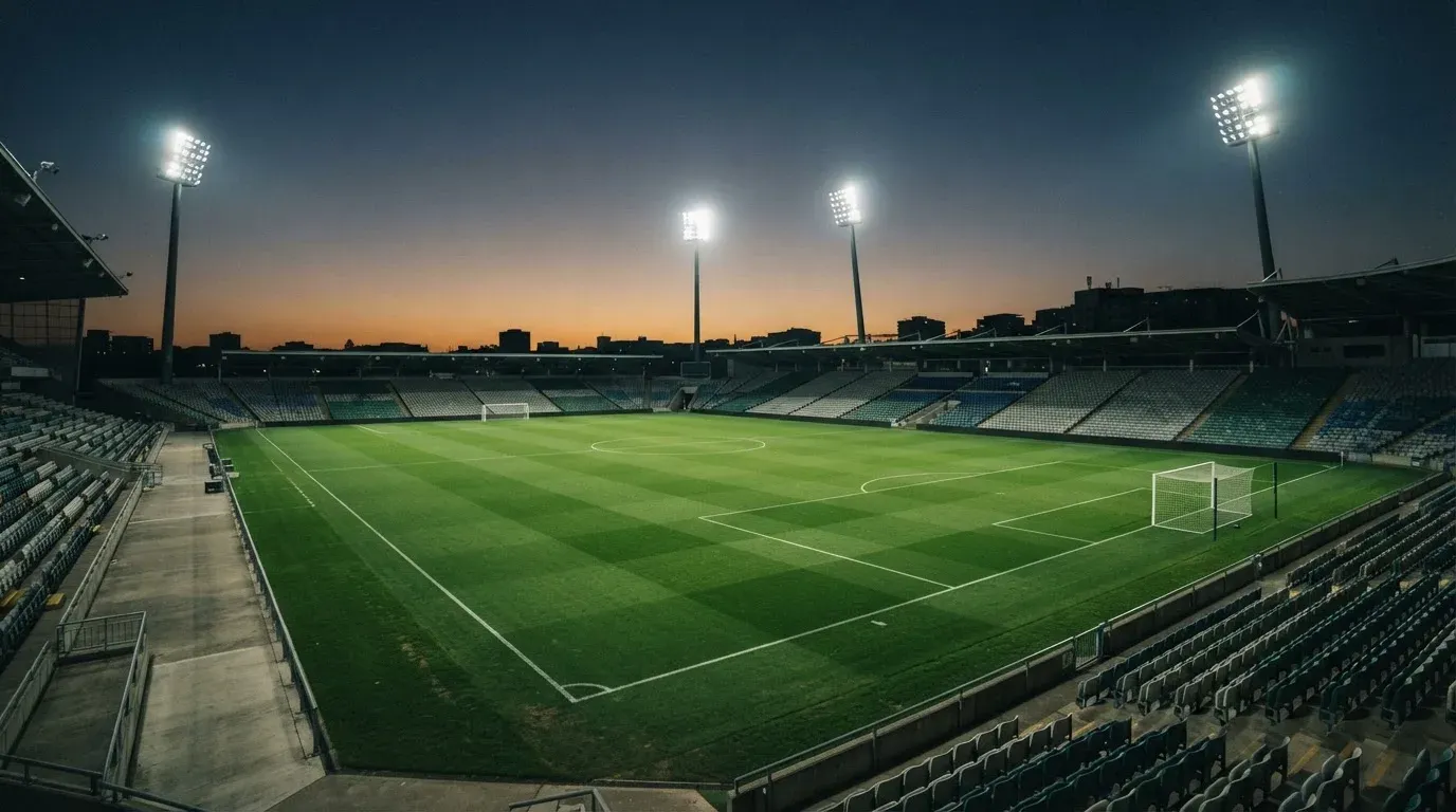An empty football stadium with floodlight masts at dusk