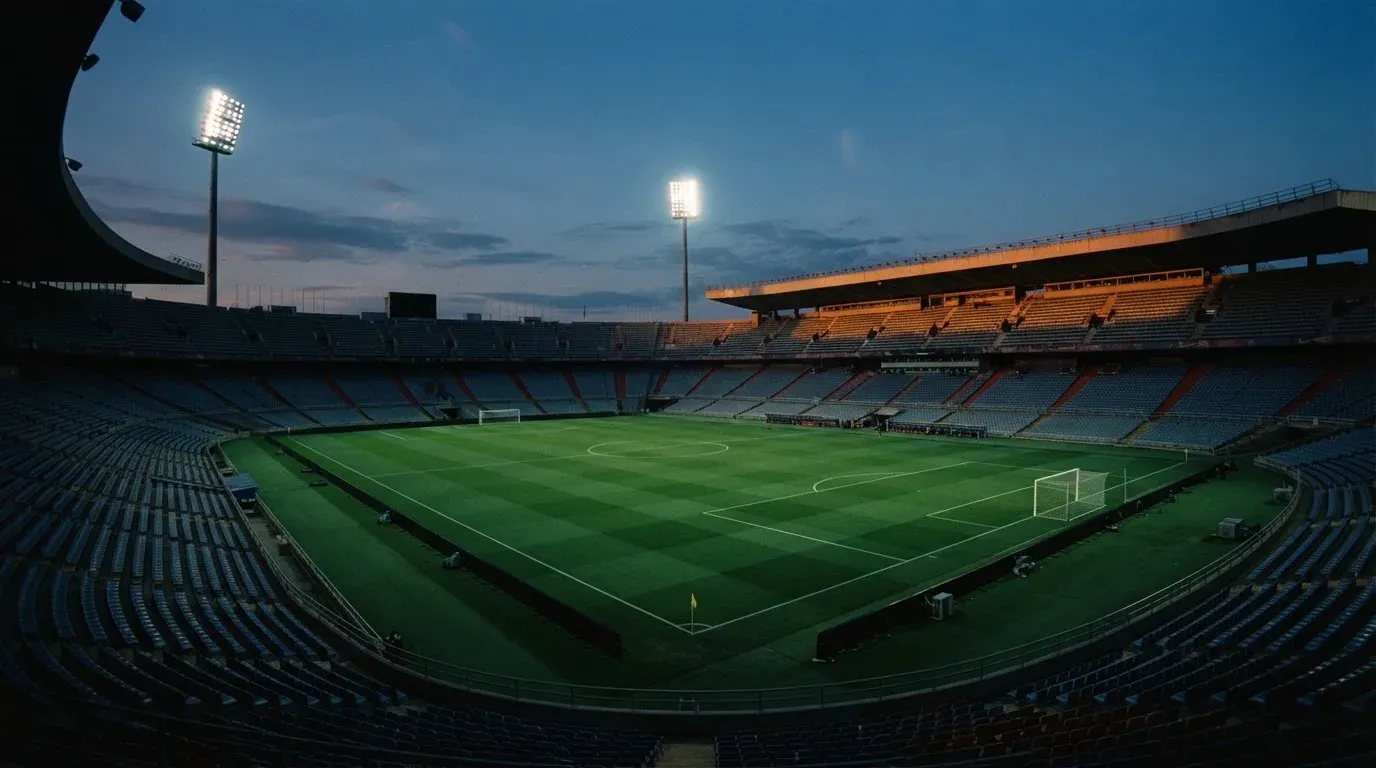An empty football stadium with floodlight masts at dusk