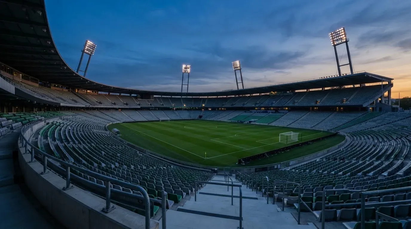 An empty football stadium with floodlight masts at dusk